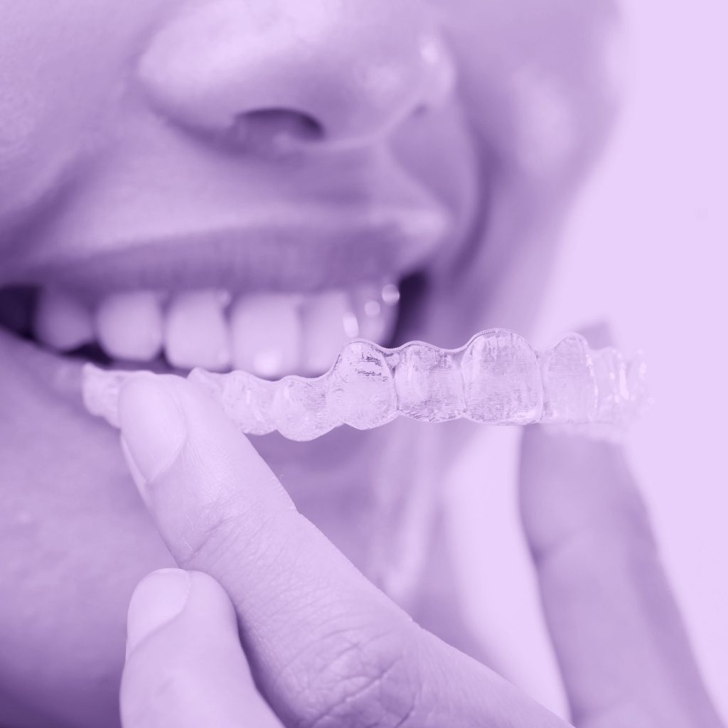 joven-mujer-sonriente-sosteniendo-aparatos-ortopedicos-invisalign-sobre-estudio-fondo-blanco-scaled